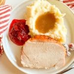 Turkey dinner plate with utensils and cranberry sauce in the background.