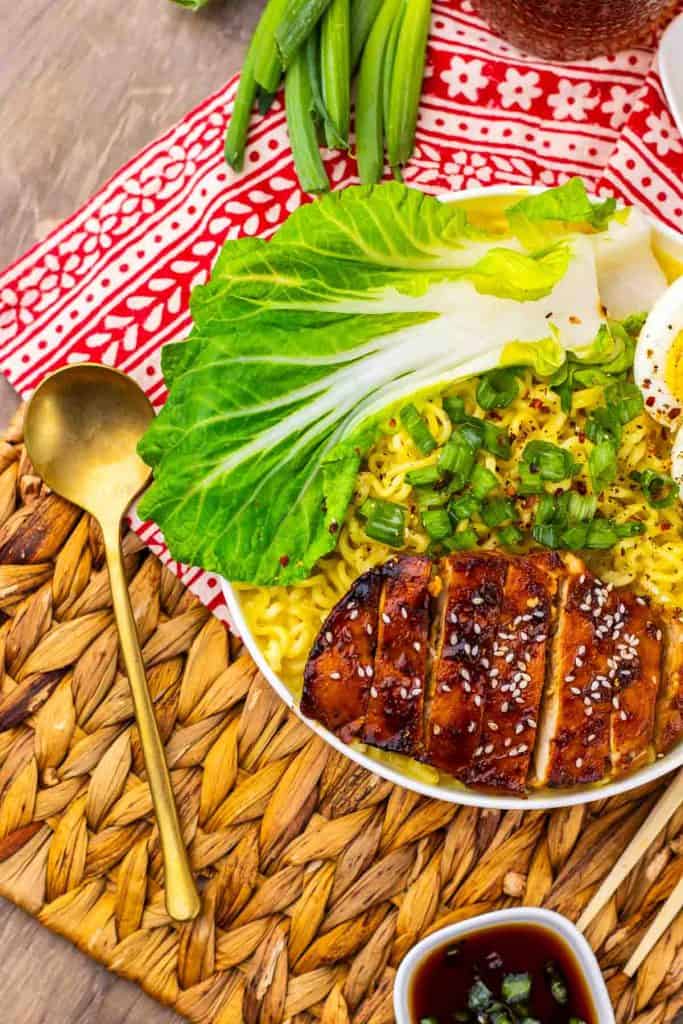 Chicken ramen topped with bok choy, scallions, and jammy eggs on a woven placemat.