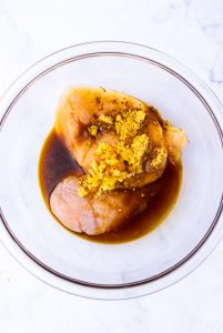 Raw chicken breasts marinating in sauce and seasonings in a bowl.