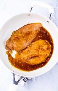 Marinated chicken breasts cooking in a skillet.