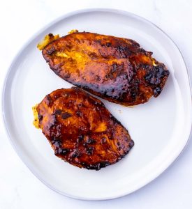 Glazed cooked chicken breasts on a white plate.
