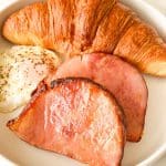 Plate with croissant, fried egg, and two ham slices.