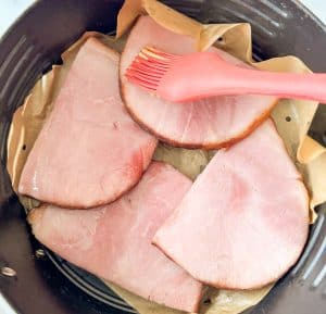 Glaze brushed over ham steaks in the air fryer basket.