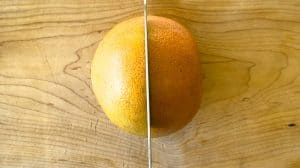 Whole grapefruit being cut in half on a cutting board for Broiled Grapefruit.