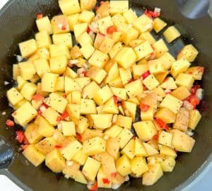 Seasoned diced potatoes, onion, and red bell pepper in a skillet for Oven Roasted Potatoes O'Brien.
