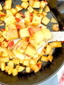 Spatula lifting Oven Roasted Potatoes O'Brien from a cast iron skillet.