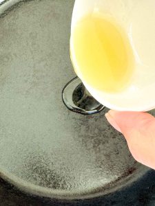 Oil being poured into a cast iron skillet for Oven Roasted Potatoes O'Brien.