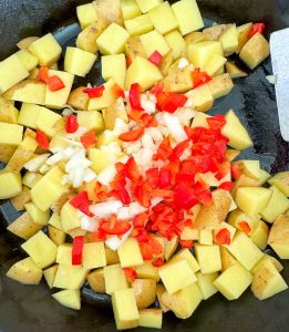 Diced potatoes, onion, and red bell pepper in a skillet for Oven Roasted Potatoes O'Brien.