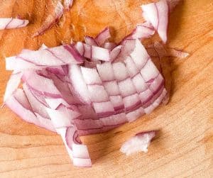 Finely chopped red onion pieces on a wooden cutting board.