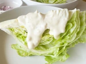 Iceberg lettuce wedge topped with creamy dressing and sprinkled with chopped red onion.
