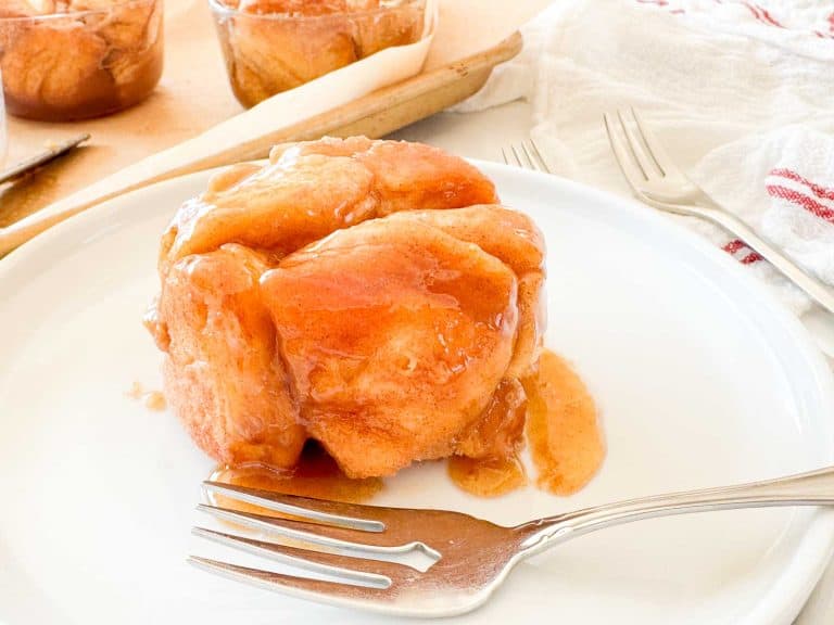 Close-up of a warm monkey bread portion on a white plate, coated in glossy caramel sauce with a fork beside it.