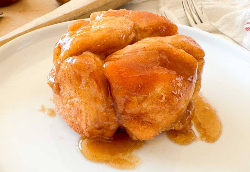 Close-up of monkey bread on a plate with glossy caramel sauce pooling around it.