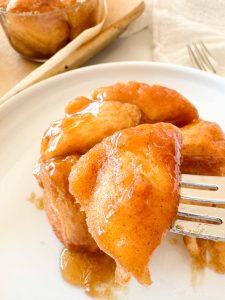 Bite of monkey bread lifted on a fork, coated in warm caramel sauce.