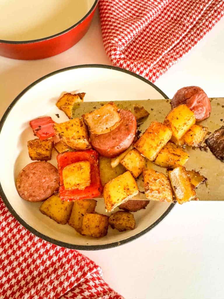 Close-up of roasted sausage slices with browned potatoes and peppers on a spatula.
