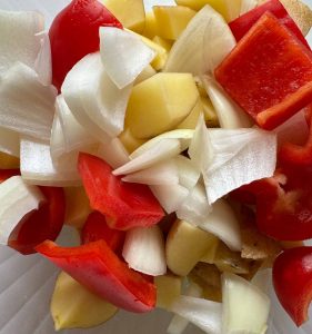 Chopped potatoes mixed with red bell pepper and onion pieces.