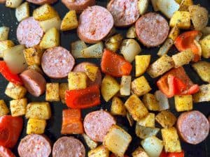 Potatoes, onions, red bell peppers, and kielbasa spread on a sheet pan with seasoning.
