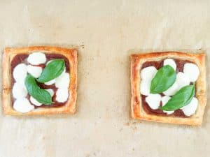 Puff pastry pizzas with melted mozzarella pearls and fresh basil leaves on top.
