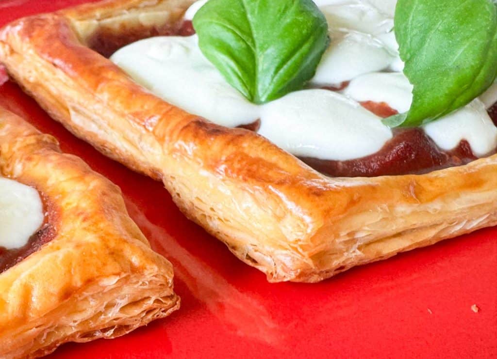 Close-up of flaky puff pastry pizza crust topped with melted mozzarella pearls and fresh basil.