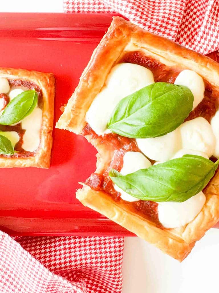Puff pastry pizza topped with mozzarella pearls and basil leaves on a red serving dish.