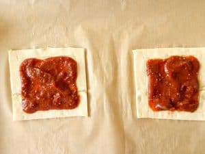 Pizza sauce spread in the center of two puff pastry rectangles before baking.