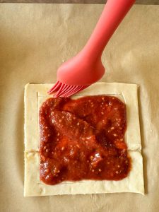 Silicone pastry brush spreading egg wash on the edges of a puff pastry pizza.