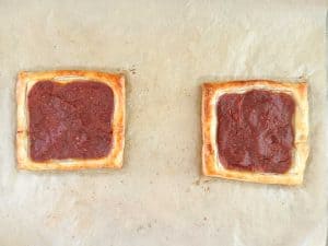 Baked puff pastry pizzas with golden edges and pizza sauce in the center on parchment paper.