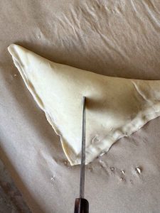 Knife cutting a small slit in the top of a prepared turnover before baking.