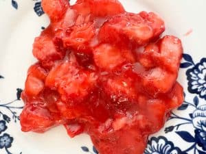 Spoonful of glossy strawberry filling on a patterned plate.